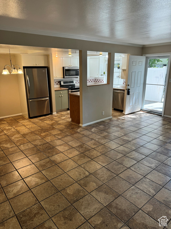 Kitchen featuring white cabinets, a textured ceiling, decorative light fixtures, stainless steel appliances, and crown molding