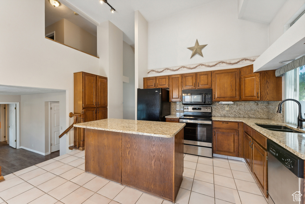 Kitchen with a high ceiling, sink, light stone counters, black appliances, and a center island