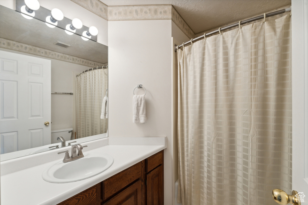 Bathroom featuring a shower with curtain, toilet, vanity, and a textured ceiling