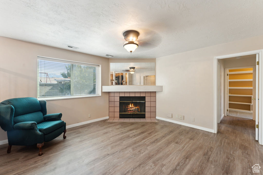 Sitting room with wood-type flooring, a textured ceiling, ceiling fan, and a tile fireplace