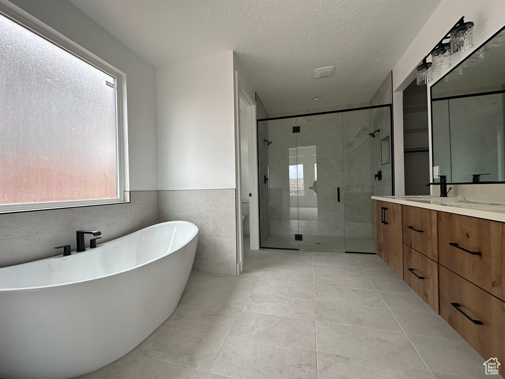 Full bathroom with tile walls, toilet, vanity, plus walk in shower, and tile patterned floors