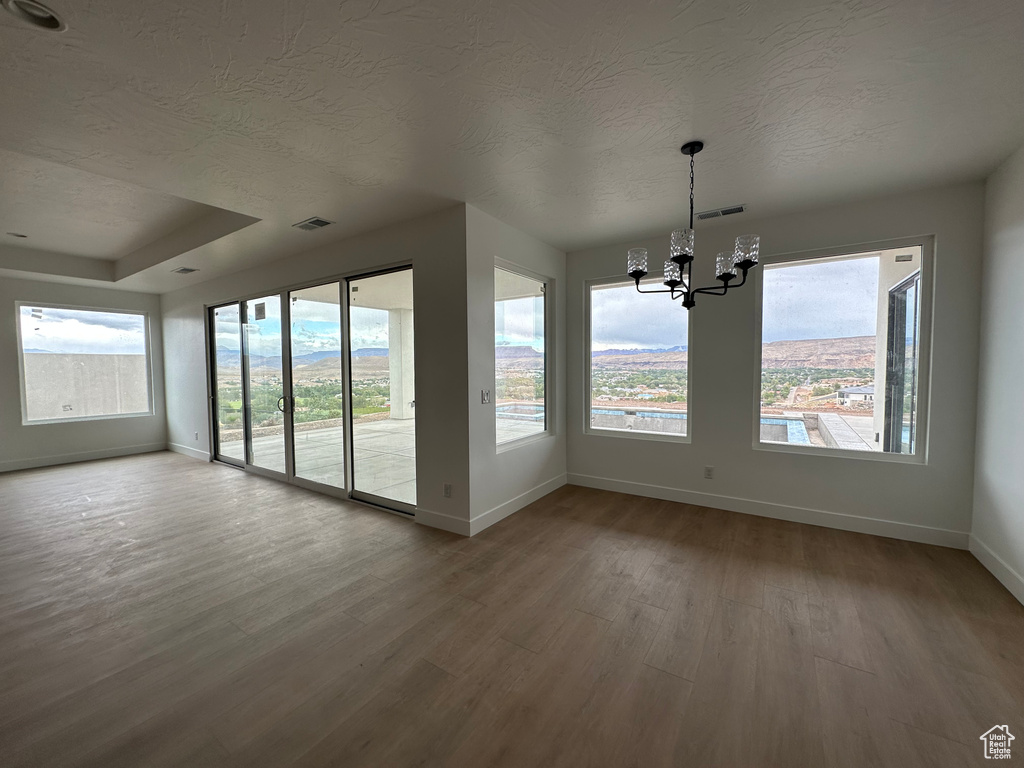 Unfurnished dining area featuring hardwood / wood-style flooring, a textured ceiling, a wealth of natural light, and an inviting chandelier