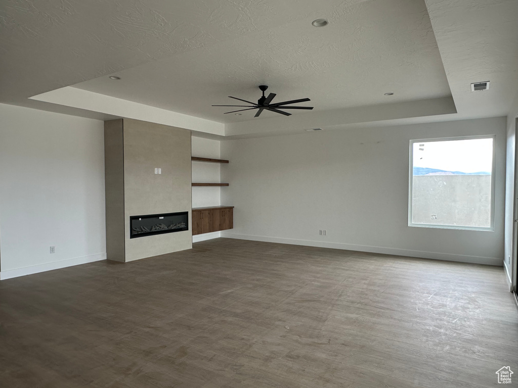 Unfurnished living room with ceiling fan, a textured ceiling, a tray ceiling, and hardwood / wood-style floors