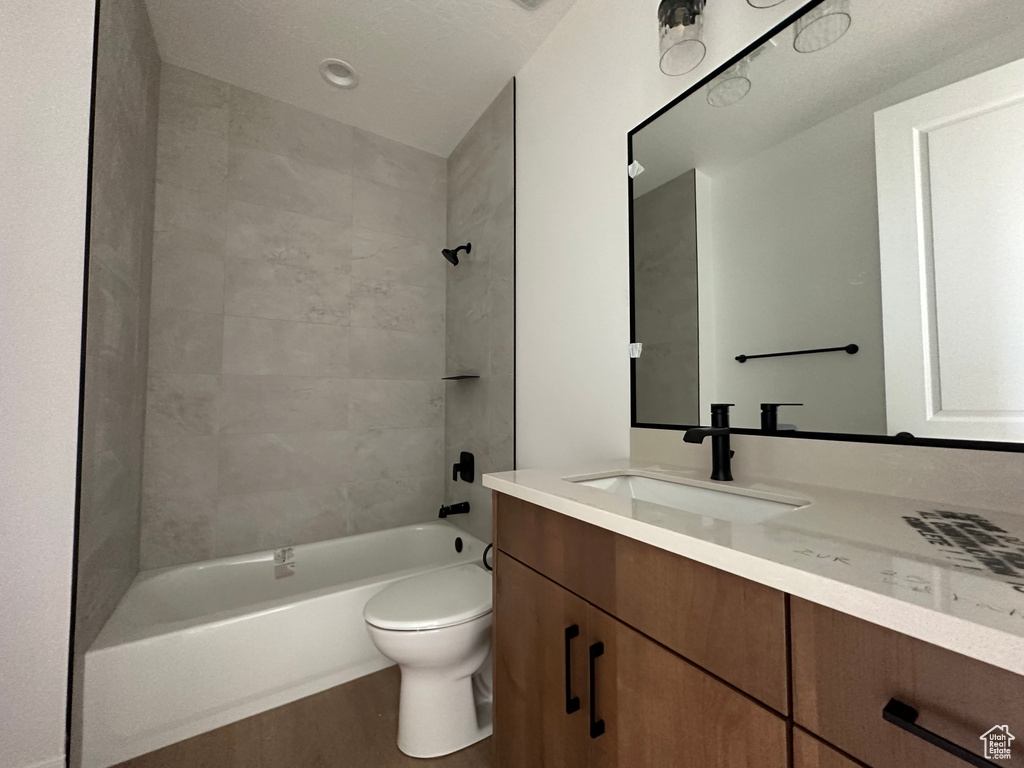 Full bathroom with vanity, toilet, tiled shower / bath combo, and a textured ceiling