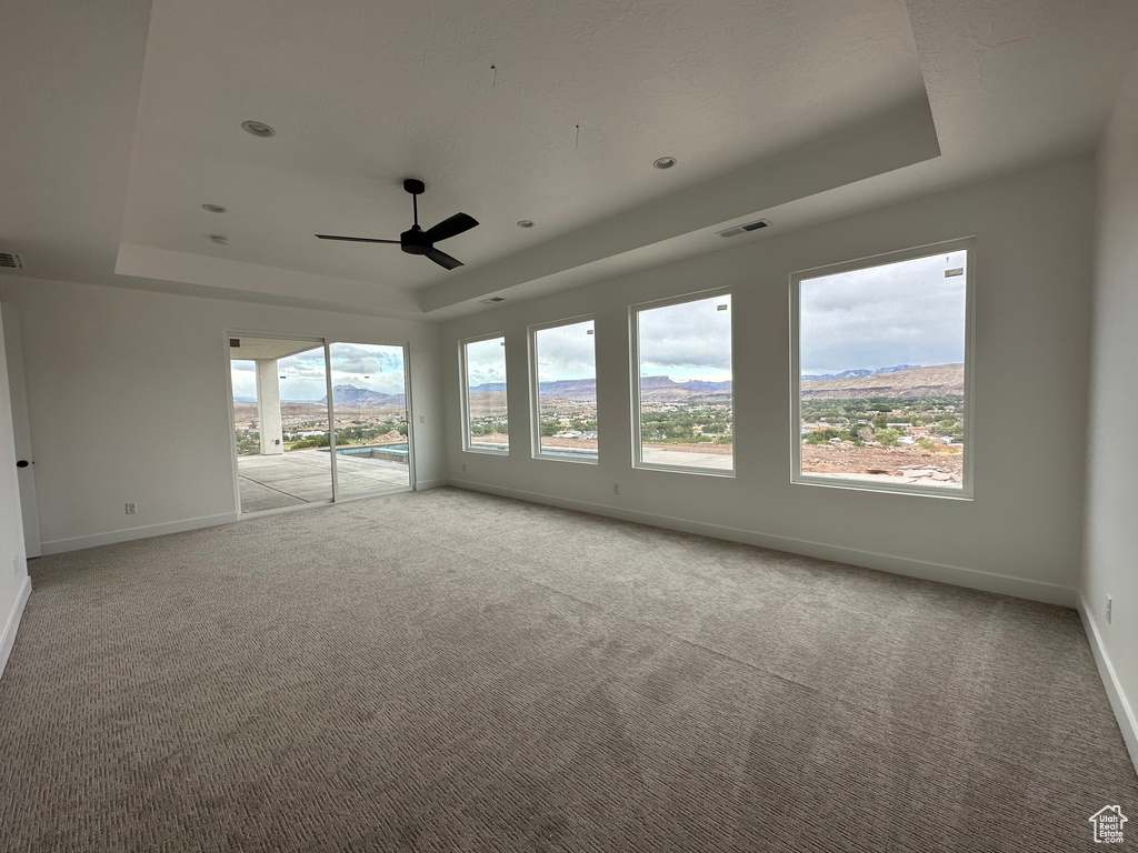 Carpeted spare room featuring ceiling fan, a mountain view, and a tray ceiling