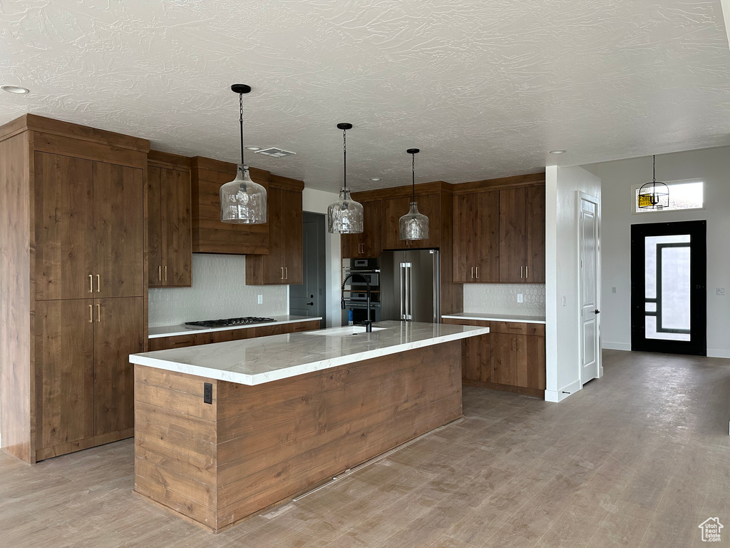 Kitchen with high end refrigerator, a center island, pendant lighting, and light hardwood / wood-style floors