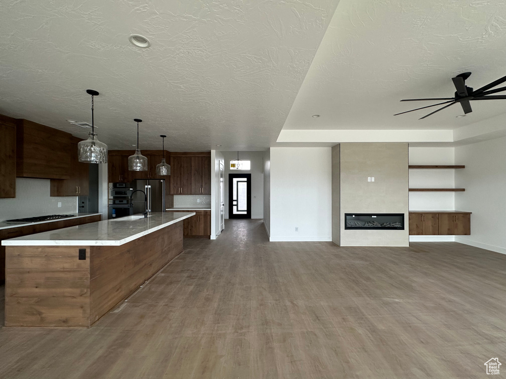 Kitchen featuring high end refrigerator, a textured ceiling, a kitchen island with sink, wood-type flooring, and decorative light fixtures