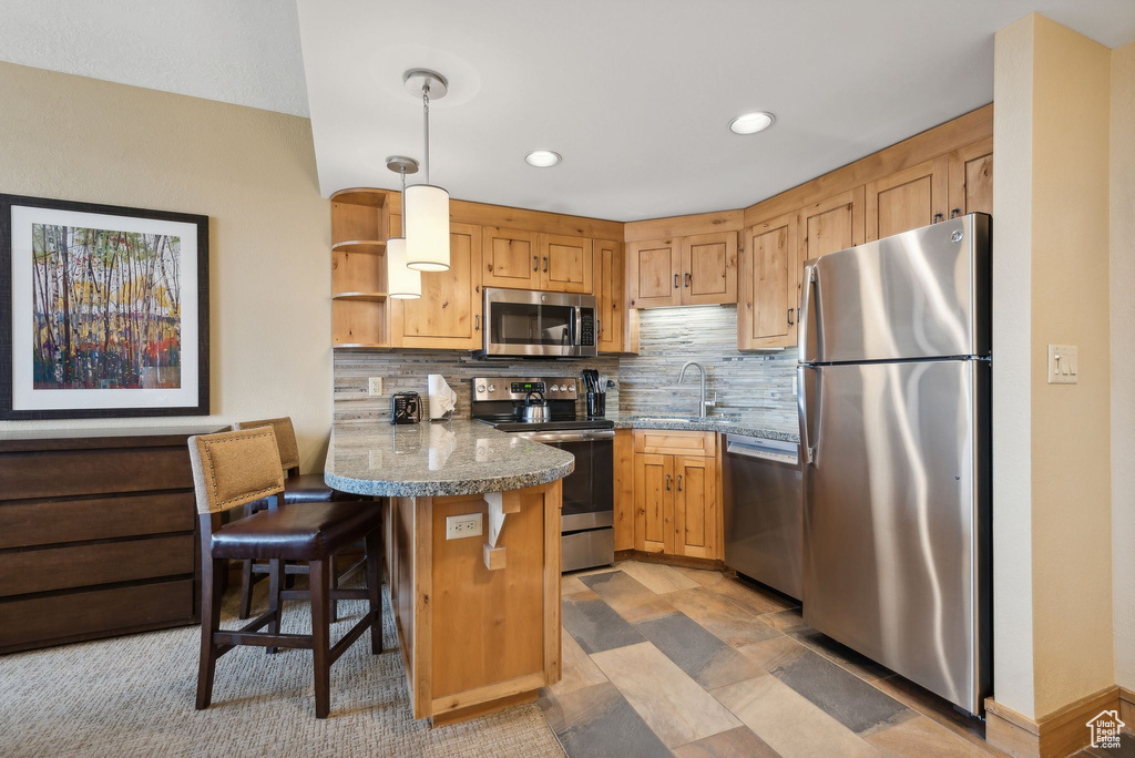 Kitchen featuring kitchen peninsula, hanging light fixtures, a kitchen breakfast bar, stainless steel appliances, and backsplash