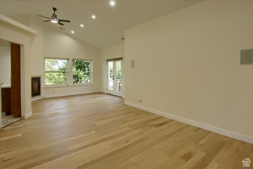 Unfurnished living room with light wood-type flooring, ceiling fan, french doors, and high vaulted ceiling