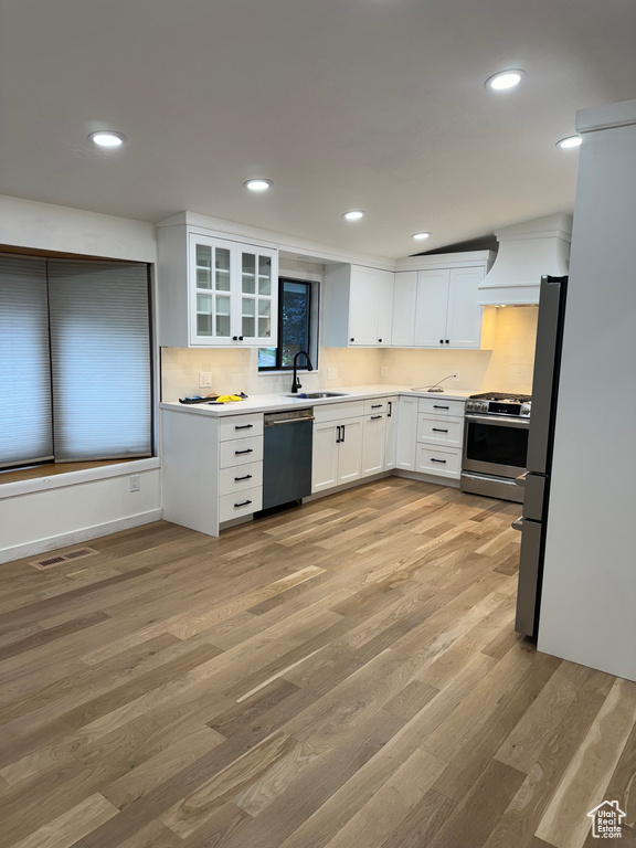 Kitchen featuring white cabinets, sink, appliances with stainless steel finishes, custom range hood, and light hardwood / wood-style floors