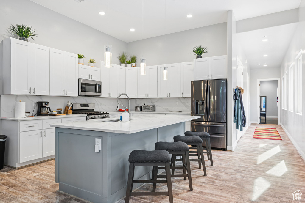 Kitchen featuring white cabinets, a center island with sink, appliances with stainless steel finishes, and light hardwood / wood-style flooring