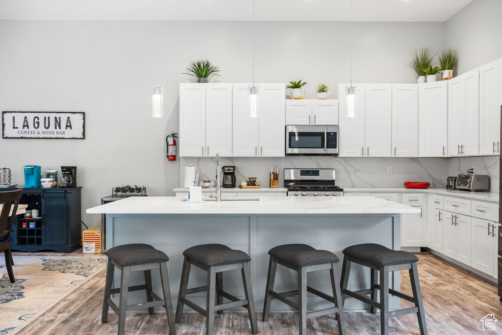 Kitchen with appliances with stainless steel finishes, white cabinetry, and an island with sink