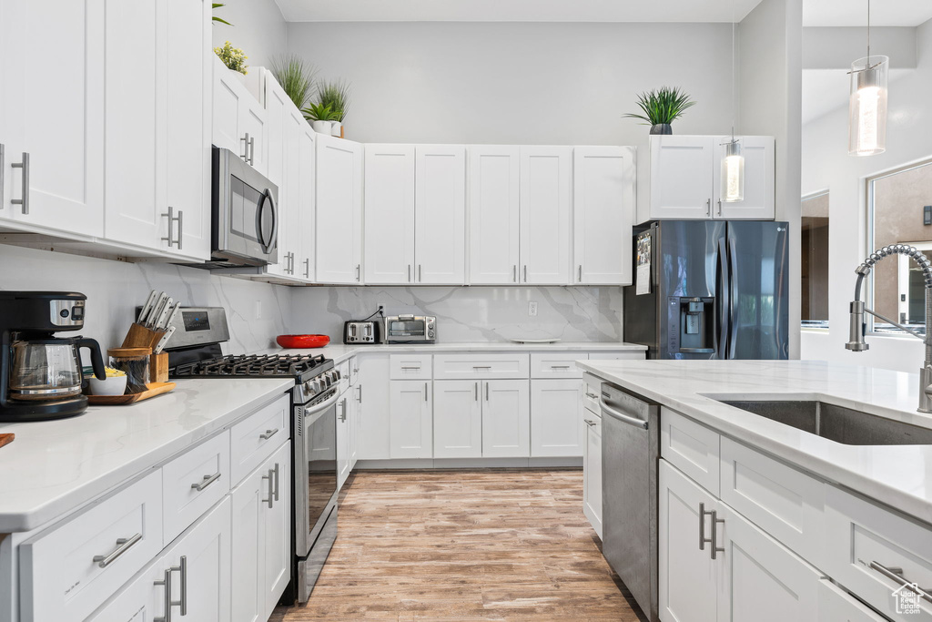 Kitchen with pendant lighting, sink, light hardwood / wood-style flooring, white cabinetry, and stainless steel appliances