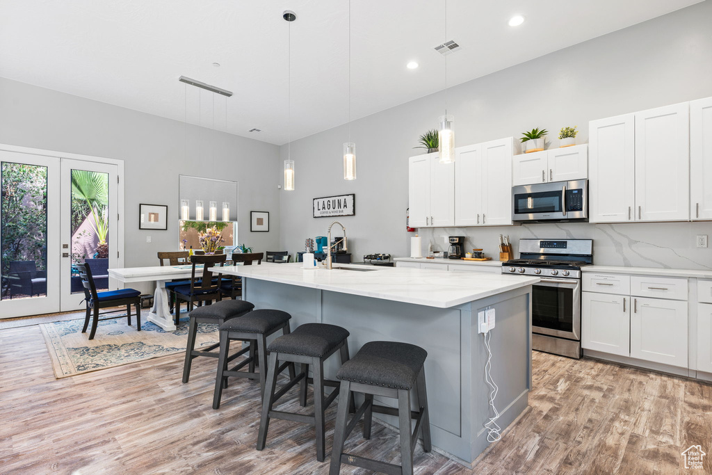 Kitchen featuring decorative light fixtures, a center island with sink, appliances with stainless steel finishes, and white cabinets