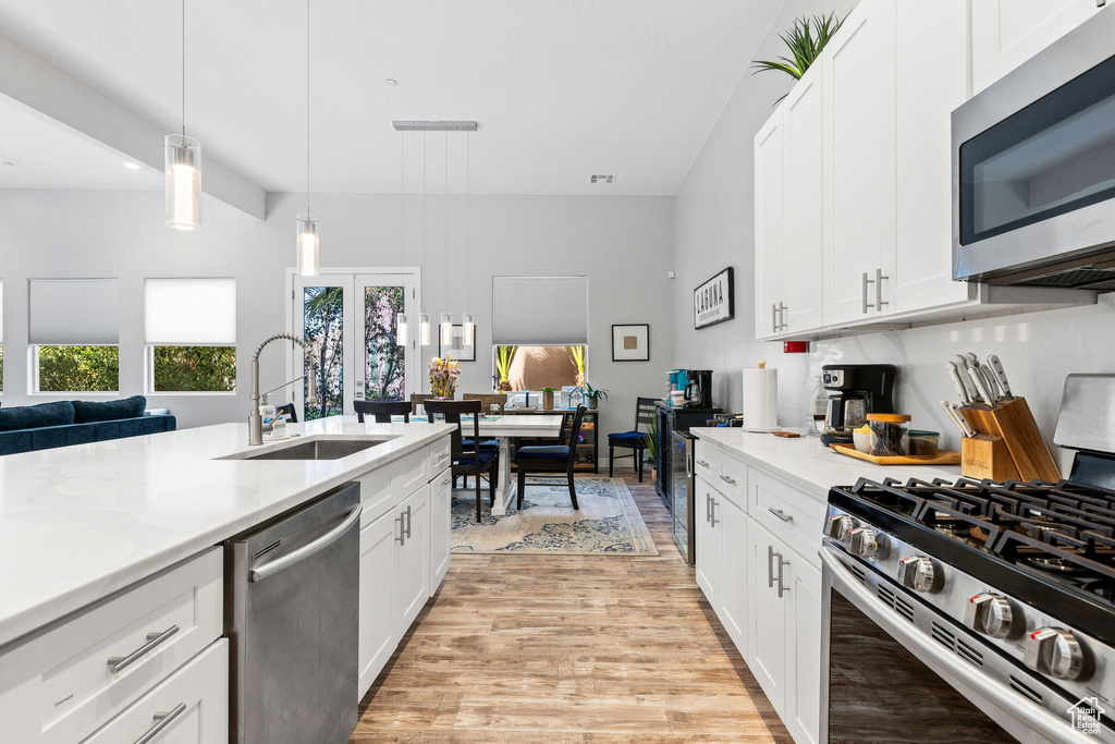 Kitchen with sink, white cabinetry, hanging light fixtures, light hardwood / wood-style flooring, and stainless steel appliances