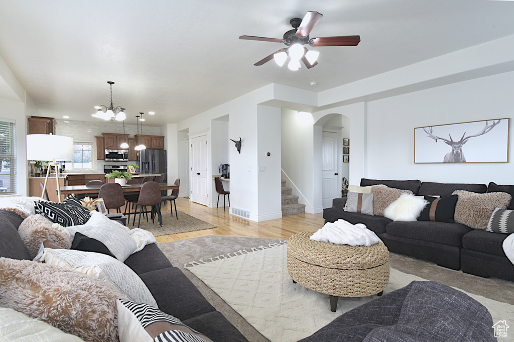 Living room featuring ceiling fan with notable chandelier and light hardwood / wood-style flooring