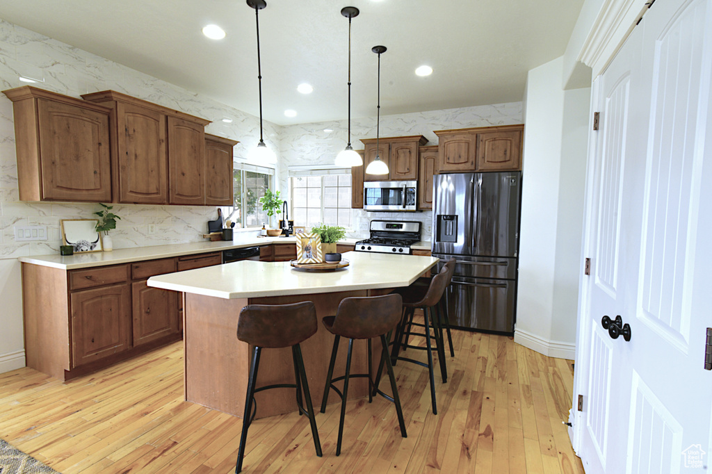 Kitchen featuring light wood-type flooring, appliances with stainless steel finishes, hanging light fixtures, and a kitchen island