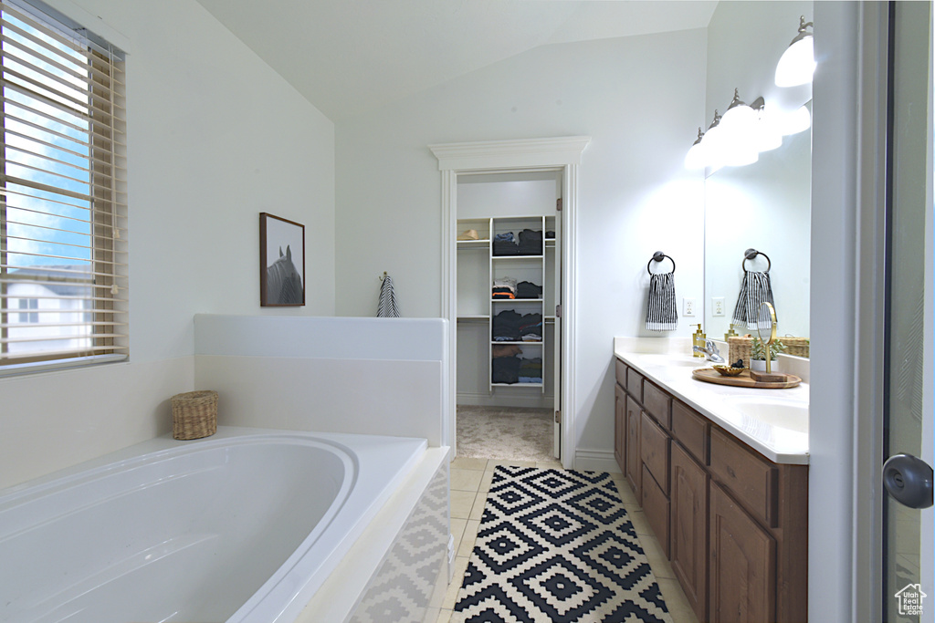 Bathroom with vanity, a relaxing tiled tub, lofted ceiling, and a healthy amount of sunlight