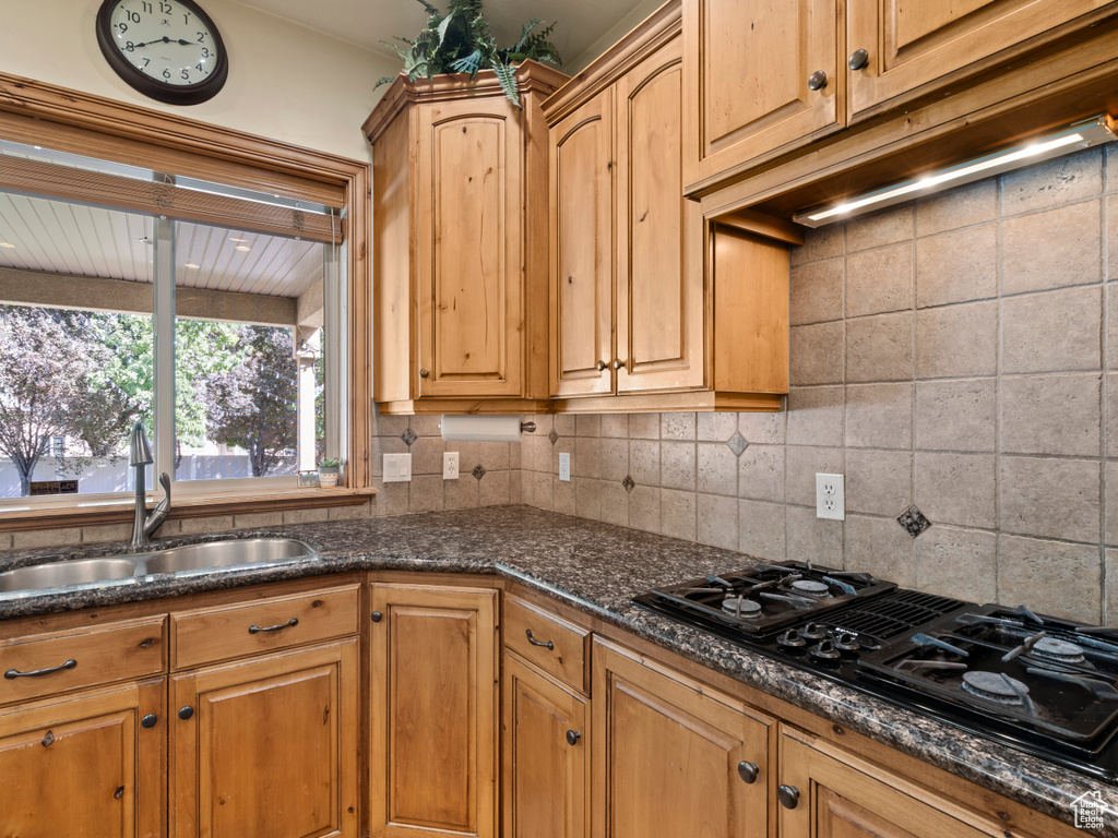 Kitchen featuring dark stone countertops, black gas cooktop, sink, and tasteful backsplash