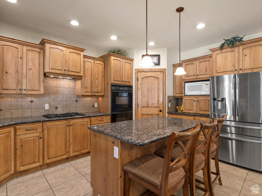 Kitchen with tasteful backsplash, a kitchen island, black appliances, light tile patterned floors, and decorative light fixtures