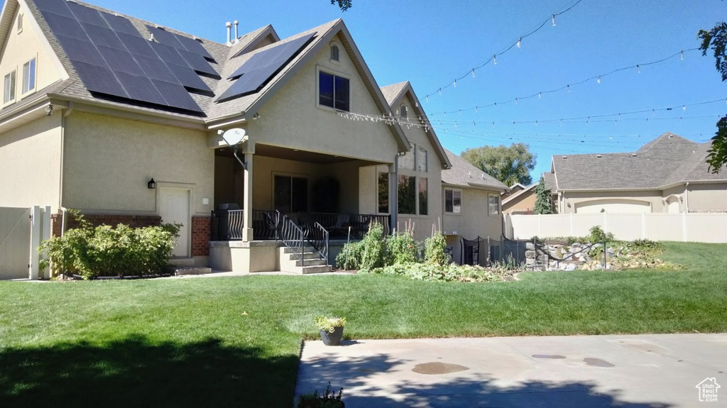 Rear view of house with a porch, solar panels, and a yard