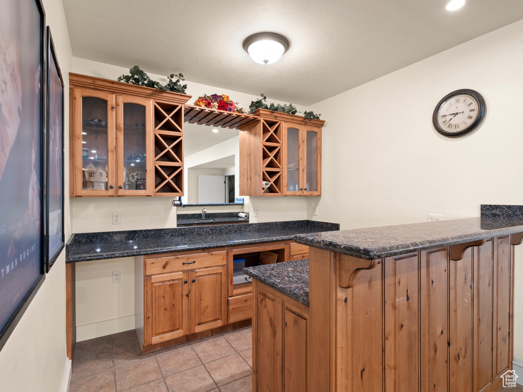 Kitchen with light tile patterned floors, dark stone counters, kitchen peninsula, and a breakfast bar