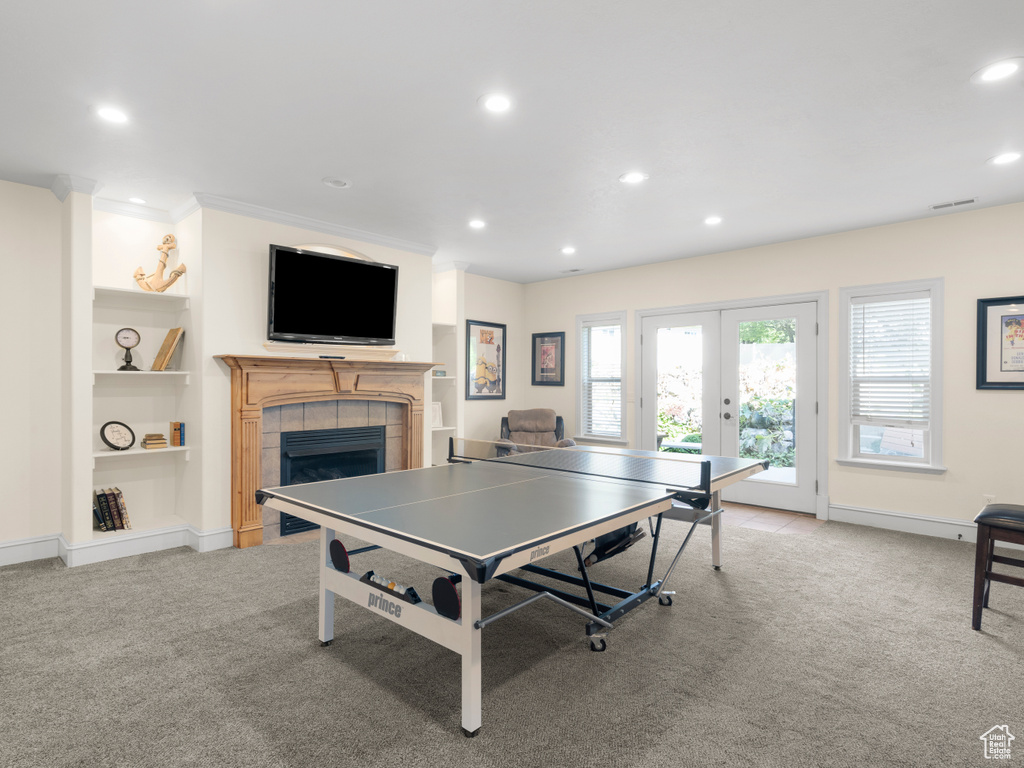 Rec room with built in shelves, french doors, light colored carpet, a fireplace, and crown molding