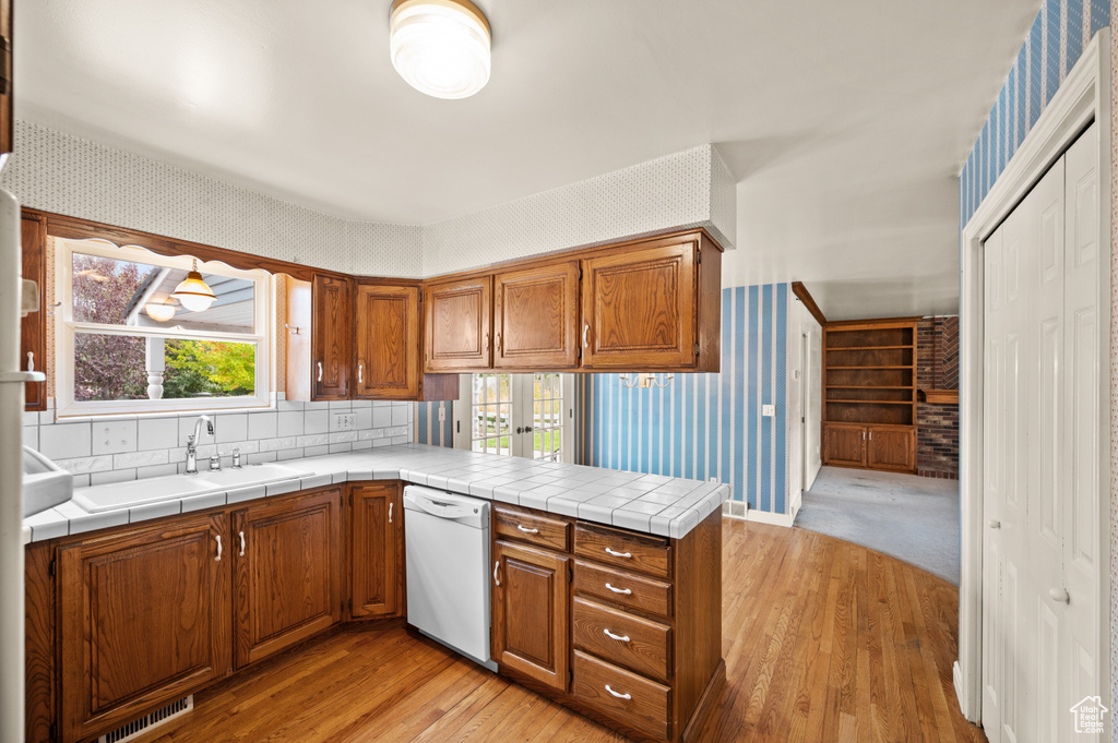 Kitchen with light wood-type flooring, dishwasher, tile counters, and a healthy amount of sunlight