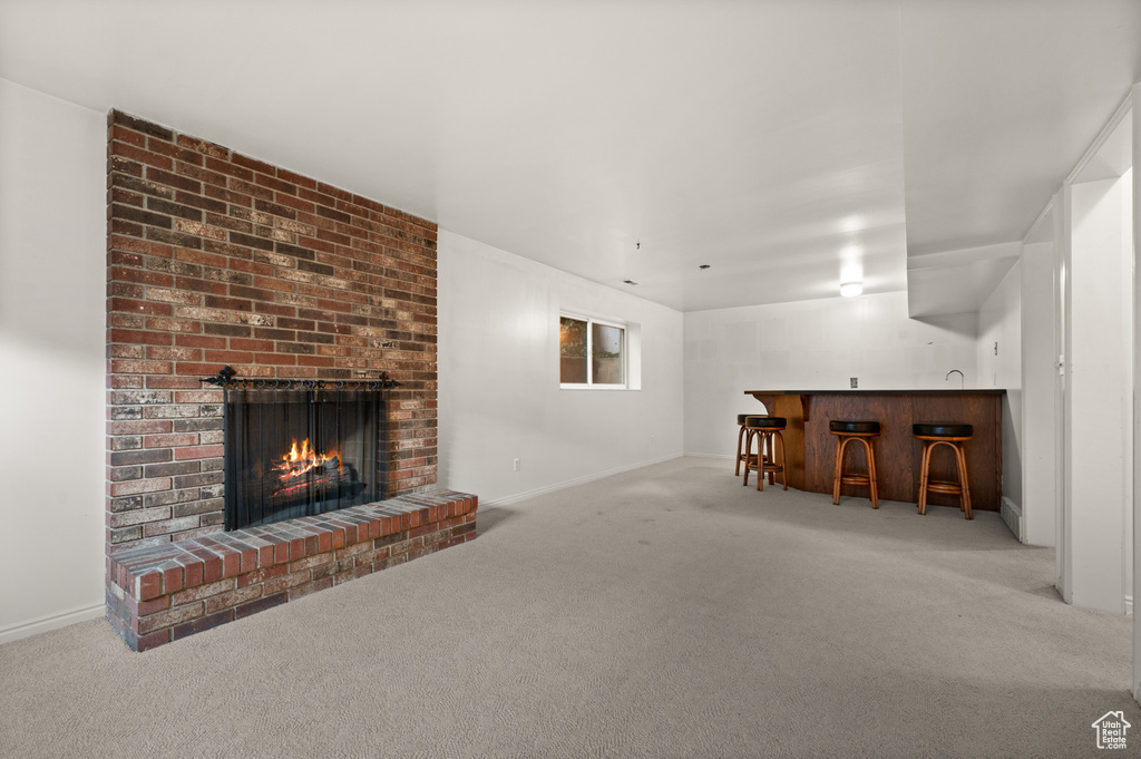 Unfurnished living room featuring light carpet, a brick fireplace, and indoor bar