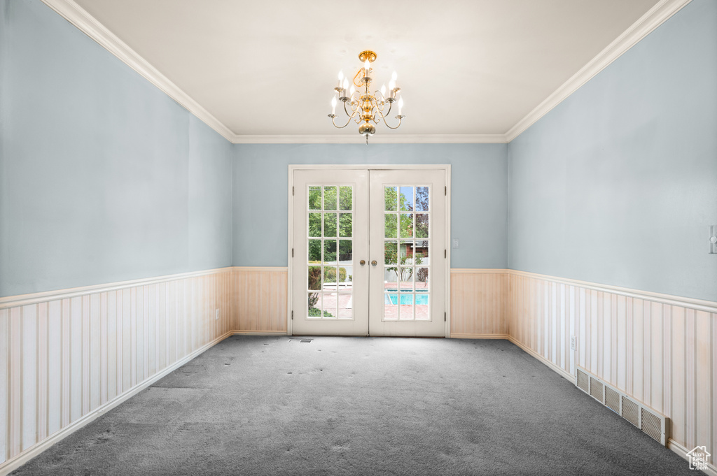 Empty room with ornamental molding, carpet, and a chandelier