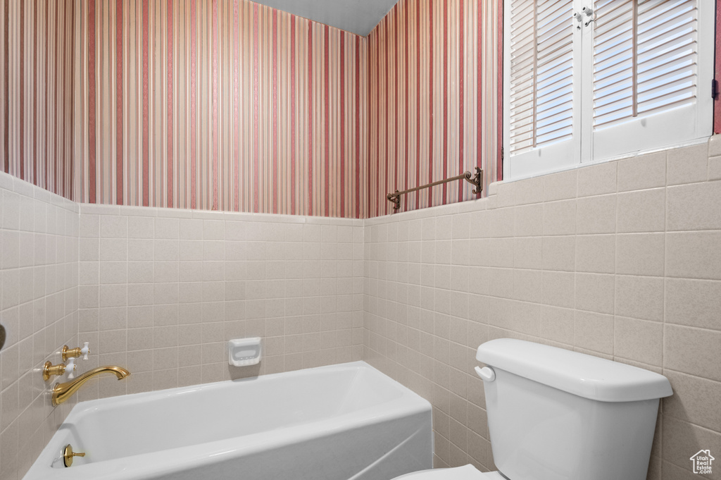 Bathroom featuring a bathing tub, tile walls, and toilet