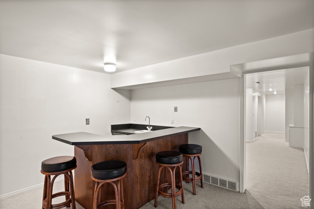 Kitchen with kitchen peninsula, sink, light carpet, and a kitchen bar