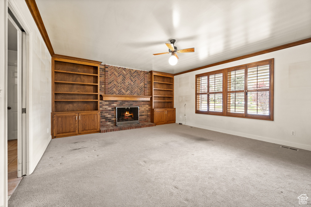 Unfurnished living room with a brick fireplace, ceiling fan, light colored carpet, and crown molding