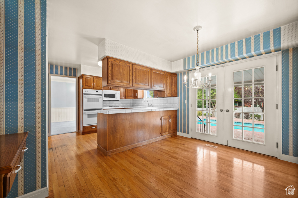 Kitchen featuring light hardwood / wood-style floors, white appliances, kitchen peninsula, french doors, and decorative light fixtures