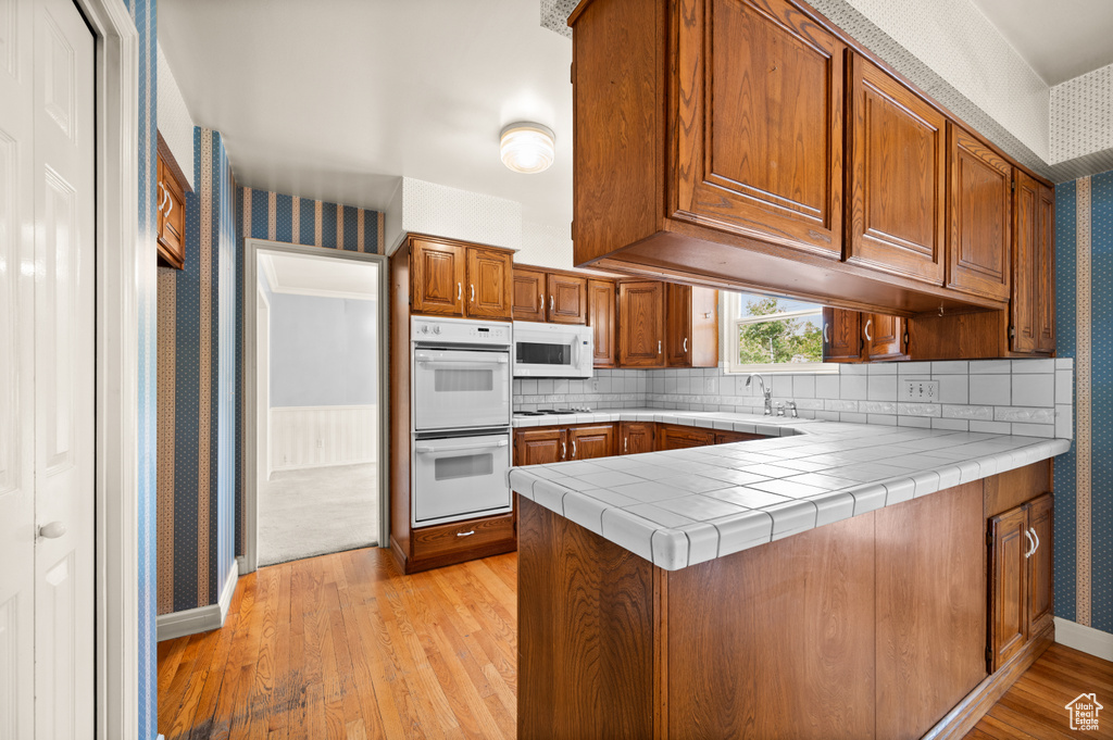 Kitchen with sink, kitchen peninsula, white appliances, light hardwood / wood-style flooring, and tile counters