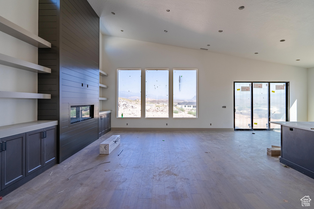 Unfurnished living room featuring light hardwood / wood-style floors, high vaulted ceiling, and a large fireplace