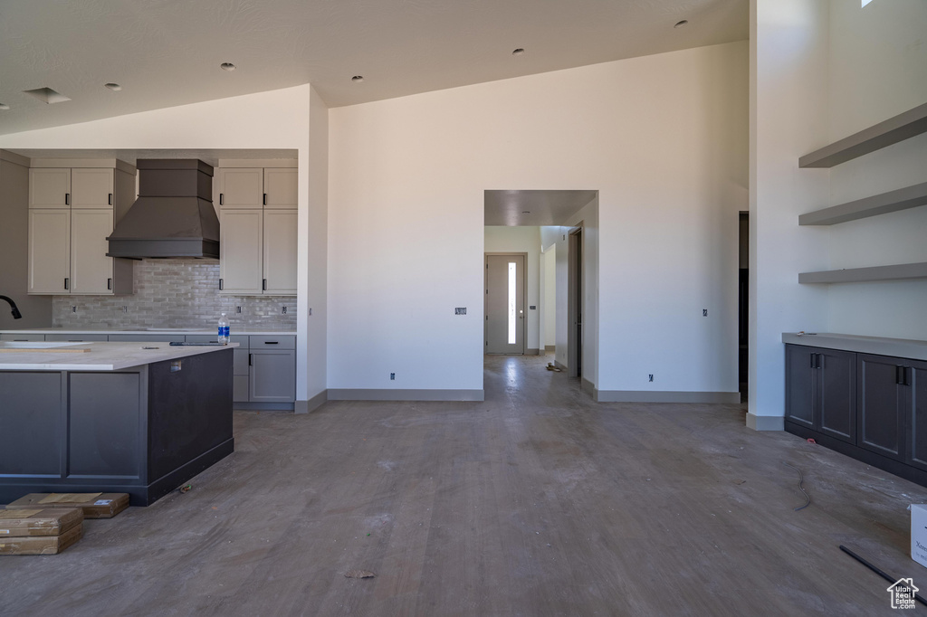 Kitchen featuring gray cabinetry, high vaulted ceiling, custom range hood, hardwood / wood-style floors, and decorative backsplash