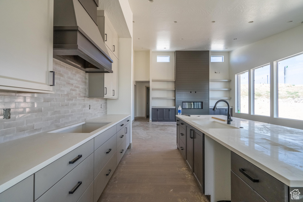 Kitchen featuring decorative backsplash, gray cabinets, wood-type flooring, custom exhaust hood, and sink