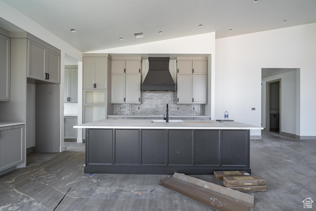 Kitchen featuring custom range hood, decorative backsplash, gray cabinets, lofted ceiling, and a center island with sink