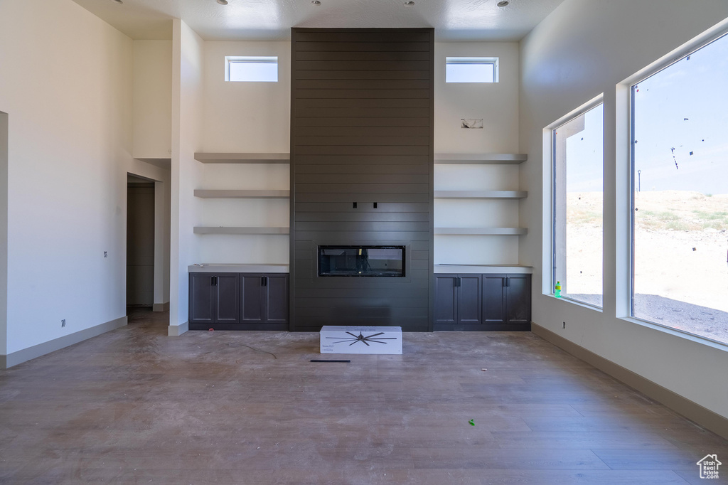 Unfurnished living room featuring a towering ceiling, a large fireplace, light hardwood / wood-style flooring, and a wealth of natural light