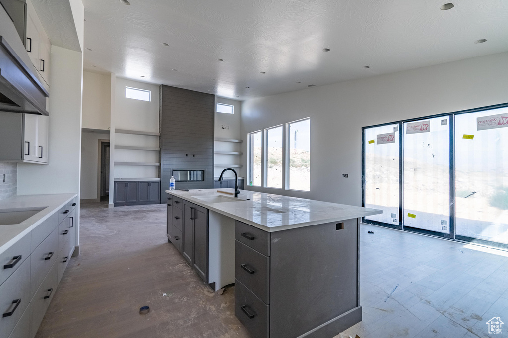 Kitchen featuring a textured ceiling, sink, an island with sink, gray cabinetry, and a large fireplace