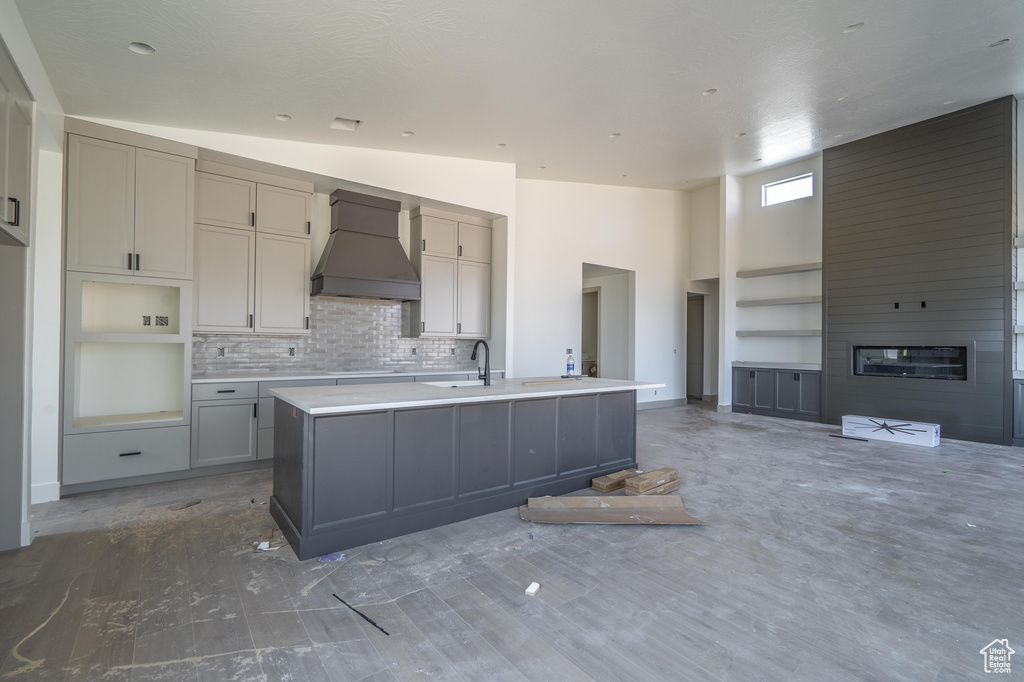 Kitchen featuring gray cabinetry, an island with sink, and custom range hood