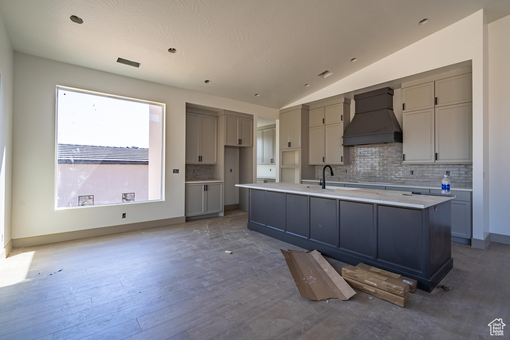 Kitchen with custom range hood, gray cabinetry, a textured ceiling, lofted ceiling, and a center island with sink