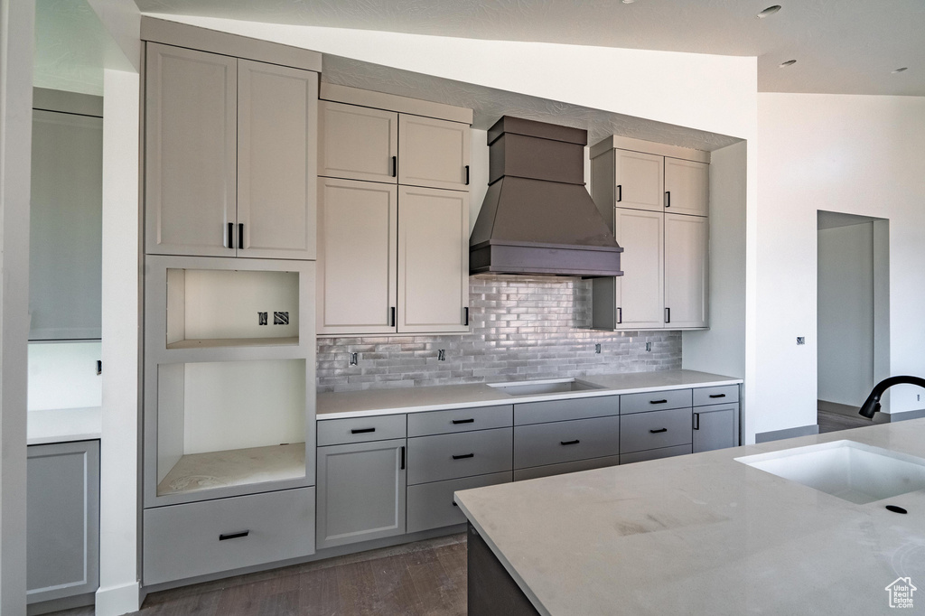 Kitchen with sink, vaulted ceiling, cooktop, custom range hood, and dark hardwood / wood-style flooring