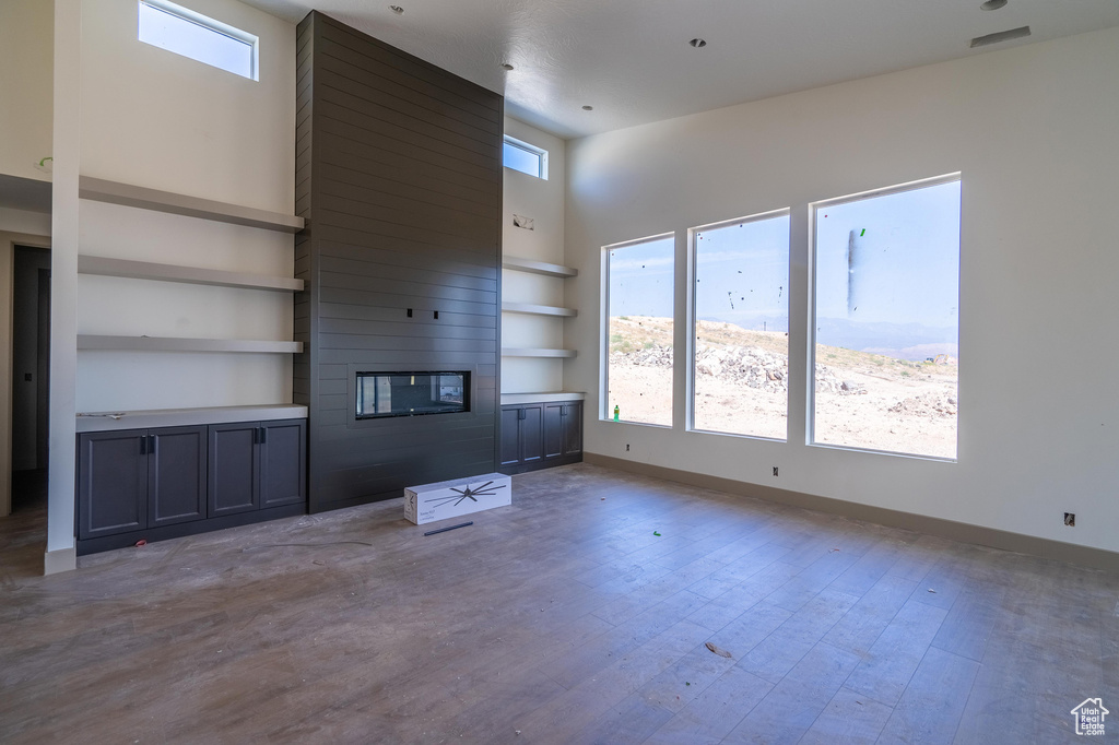 Unfurnished living room with light wood-type flooring, a healthy amount of sunlight, a fireplace, and a towering ceiling