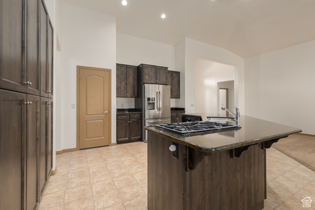 Kitchen with a kitchen breakfast bar, an island with sink, dark stone counters, sink, and appliances with stainless steel finishes