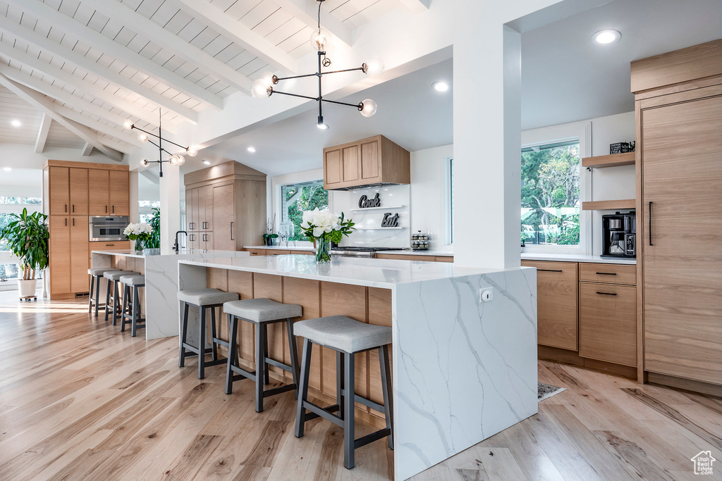 Kitchen featuring vaulted ceiling with beams, light hardwood / wood-style floors, a large island with sink, and a chandelier