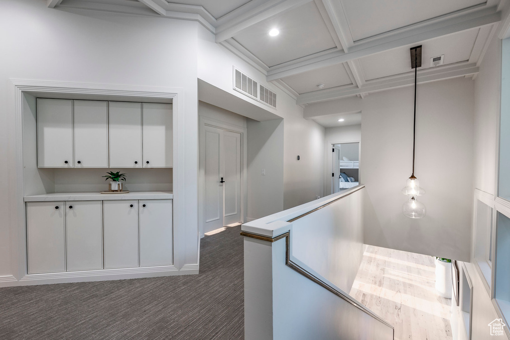 Corridor with coffered ceiling, crown molding, beam ceiling, and dark carpet