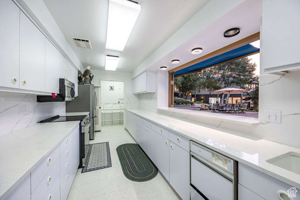 Kitchen with light stone countertops, appliances with stainless steel finishes, backsplash, and white cabinetry