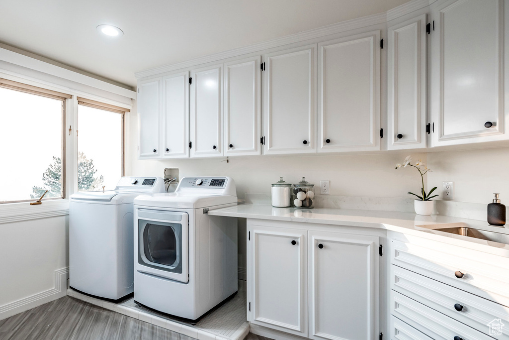 Laundry area featuring washer and clothes dryer, light hardwood / wood-style floors, sink, and cabinets